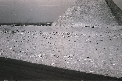 Black-and-white aerial view of the Great Pyramid of Giza, showcasing its massive limestone base and surrounding desert terrai...