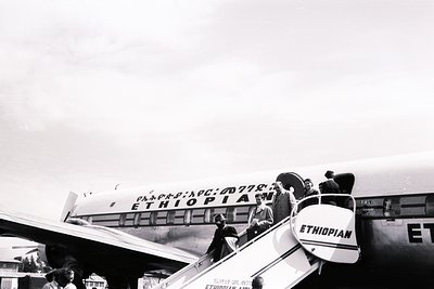 Passengers disembarking Ethiopian Airlines aircraft, mid-20th century. Classic 1950s–60s jet bridge and propeller plane with ...