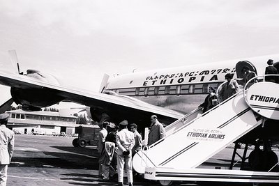 Ethiopian Airlines DC-6B aircraft with "ETHIOPIA" and "Ethiopian Airlines" branding, mid-20th century. Passengers disembark v...