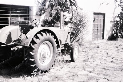 Vintage tractor plowing field, likely mid-20th century. Classic design with large rear wheels and exposed engine components. ...