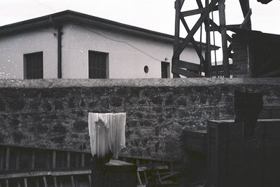 Industrial-era laundry setup with wet fabric hanging on a stone ledge. Plain brick building with a rusted metal structure in ...