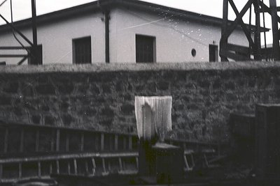 Industrial-era brick wall with rusted metal railings and a faded white building in background. Likely a mid-20th-century fact...