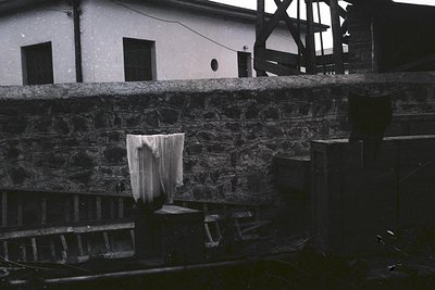 Black-and-white shot of a weathered stone wall with draped fabric, likely a curtain or sheet, hanging over a concrete ledge. ...