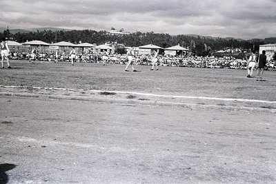 Black-and-white photo of a mid-20th century baseball game in a rural setting, likely 1940s-1950s. Players in vintage uniforms...