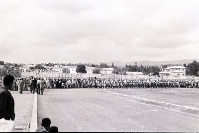 Black-and-white photo of a large outdoor gathering, likely a public event or rally. Dense crowd of people in uniform or coord...