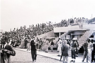 Black-and-white photo of a large crowd gathered on a stone terrace, likely a public event or demonstration. Uniformed officia...