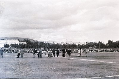 Vintage black-and-white photo of a large-scale outdoor sports event, likely a 1950s–1960s track meet. Crowds line the perimet...
