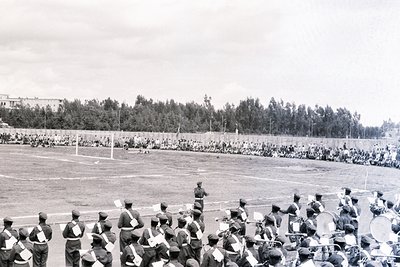 Black-and-white photo of a large-scale military parade on a grassy stadium field, likely mid-20th century. Uniformed soldiers...