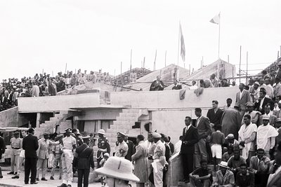 Black-and-white photo of a mid-20th-century public event at a stadium or amphitheater. Crowds gather on tiered concrete seati...