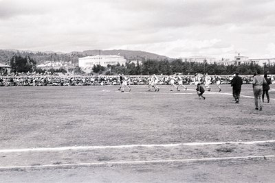 Black-and-white shot of a mid-20th-century soccer match in an open stadium, likely Eastern Bloc era. Players in light uniform...
