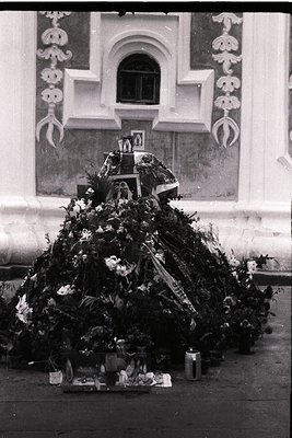 Vintage funeral wreath adorned with flowers, ribbons, and framed photos, placed against a decorative church facade with arche...