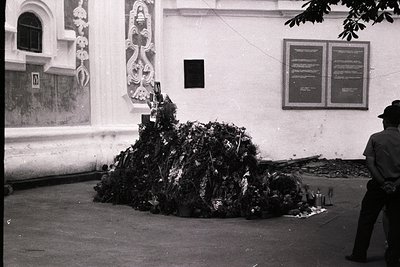 A black-and-white street scene featuring a makeshift memorial or shrine composed of bundled fabric, ropes, and debris piled a...