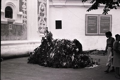 Black-and-white street scene featuring a makeshift memorial of bundled flowers, ...
