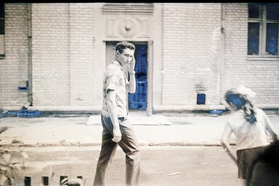 Vintage sepia-toned street scene featuring a man in a short-sleeved button-up shirt and trousers, holding a phone to his ear ...