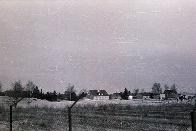 Vintage black-and-white rural landscape featuring modest brick houses with pitched roofs, surrounded by open fields and spars...