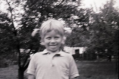 Blurred black-and-white portrait of a smiling child in a short-sleeve shirt, mid-20th century. Soft focus and motion blur sug...