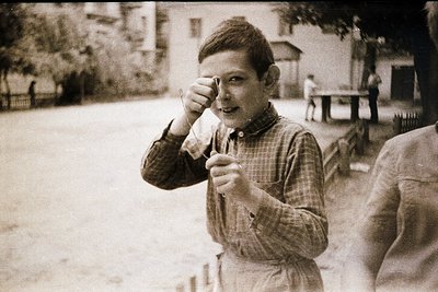 Mid-20th century boy in plaid shirt and shorts holding a cone of ice cream, mid-laugh. Urban park setting with blurred backgr...