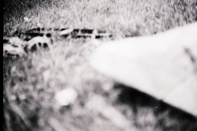Vintage black-and-white close-up of a **chain-link fence** with **snow accumulation**, likely urban/suburban setting. Distort...