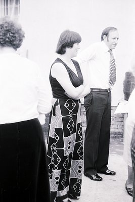 1970s indoor gathering with three individuals in formal attire. Woman in geometric-patterned dress with geometric motifs, man...