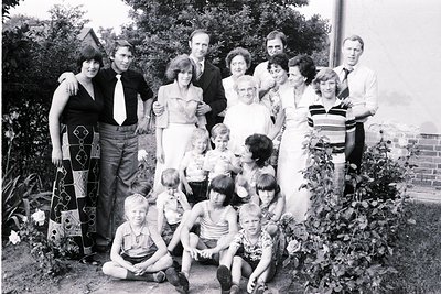 Family portrait from the **1970s**, featuring adults in formal attire (ties, dresses) and children in casual summer wear. Lus...