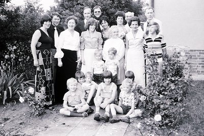Family portrait in a lush garden setting, likely mid-20th century (1960s–1970s). Three generations pose on stone steps surrou...