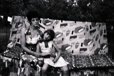 Two women pose in a 1960s/70s outdoor setting, framed by abstract, geometric wallpaper. The woman on left wears a sleeveless ...