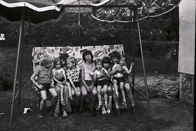 Vintage black-and-white photo of six children posing under a striped canopy, likely from the **1960s–1970s**. Casual summer a...