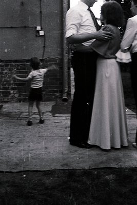 Mid-20th century urban alleyway scene: a child in short pants and striped shirt throws a ball, while adults in formal attire ...