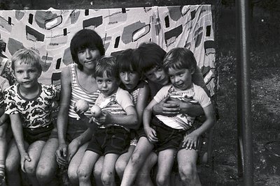 Black-and-white portrait of a woman and five children posing closely together, likely 1960s–1970s. The woman wears a striped ...