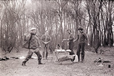 Four men in 1970s outdoor camping attire—flannel shirts, jeans, and hats—pose in a leafless forest clearing. Foldable camping...