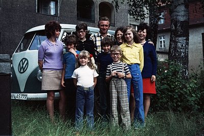 Family portrait in front of a 1960s–1970s Volkswagen Type 2 (VW Bus) with "VN-AS777" license plate. Eight individuals pose ou...