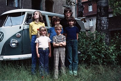 Vintage 1970s family portrait beside a silver VW Type 2 (Bus) with "77" badge. Five children and two adults in casual 70s att...