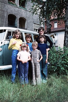 Five children pose outdoors in 1970s European suburban style—flared jeans, striped shirts, and bold hairstyles. A vintage Vol...