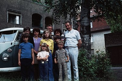 Family portrait in front of a vintage Volkswagen van, likely late 1970s–early 1980s. Eight individuals pose outdoors near a r...