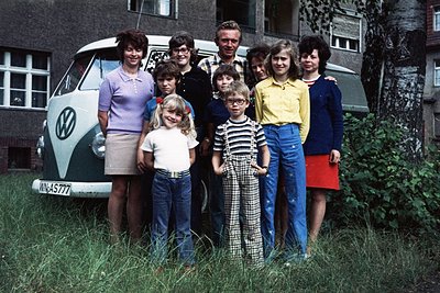 Family portrait in front of a **Volkswagen Type 2 (VW Bus) "Bullshit" model**, likely **1970s**. Eight individuals pose in ca...