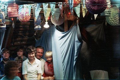 Vintage family portrait in a dimly lit, festive indoor setting with paper lanterns and string lights. Group of 8 people—adult...