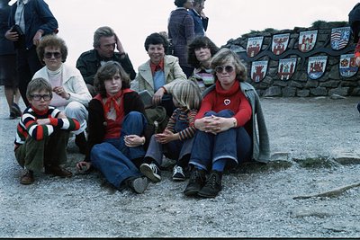 Group of 10 people posing outdoors, 1970s. Adults in flared jeans, sweaters, and blazers; children in striped shirts and bell...