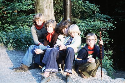 Vintage group portrait of five individuals in a wooded area, likely 1970s. Casual attire includes bell-bottoms, sweaters, and...
