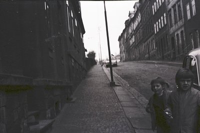 Vintage black-and-white street scene featuring narrow alleyway flanked by multi-story brick buildings with classic European a...