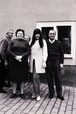 1960s-70s family portrait in Eastern Bloc-style residential courtyard. Four adults pose in front of a modest brick building w...