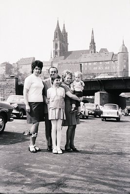 Family portrait in front of a Gothic-style cathedral with twin spires, likely **1960s Europe**. Four adults and a child pose ...