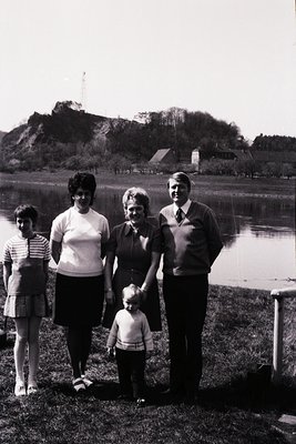 Family portrait by a serene lakeside with rocky hill in background, likely . Four adults and a child pose in casual outdoor a...