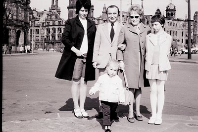 Family portrait in front of Berlin’s iconic **DDR Parliament Building** (now Reichstag), 1960s–1970s. Four adults and a child...
