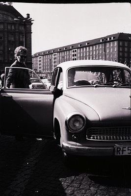 Vintage 1960s-era car (likely a Morris Oxford or similar) parked on a cobblestone street in an urban setting. A person in a l...