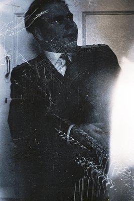 Vintage sepia-toned portrait of a man in a dark suit, tie, and white shirt, captured through a scratched glass window. Light ...