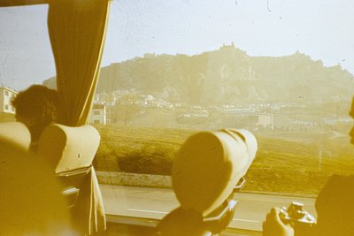 Vintage sepia-toned train window view showing two passengers gazing at a rocky hilltop fortress. Mid-20th century European co...