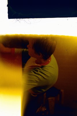 Vintage Polaroid-style photo of a seated person in profile, blurred by light exposure. Warm sepia tones dominate, with a yell...