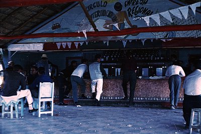 Vintage bar interior with 1970s-era patrons. Wooden bar counter displays shelves of bottles, framed by decorative murals and ...