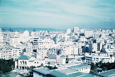 Vintage aerial view of a densely built Mediterranean cityscape, featuring mid-20th century architecture with flat roofs and l...