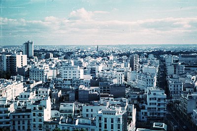 Vintage aerial view of a densely built urban landscape with mid-rise concrete buildings, likely from the 1960s–1970s. Promine...